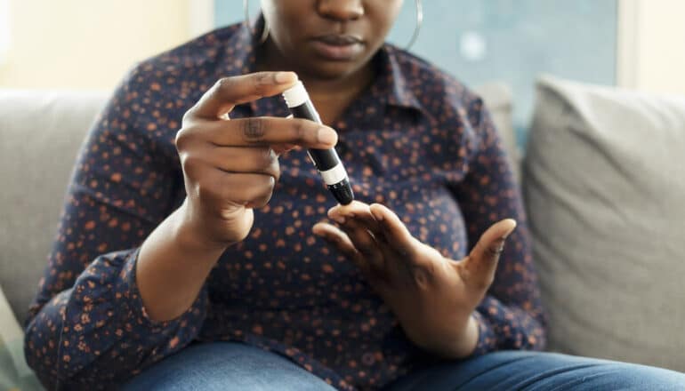 person tests blood sugar while seated on couch