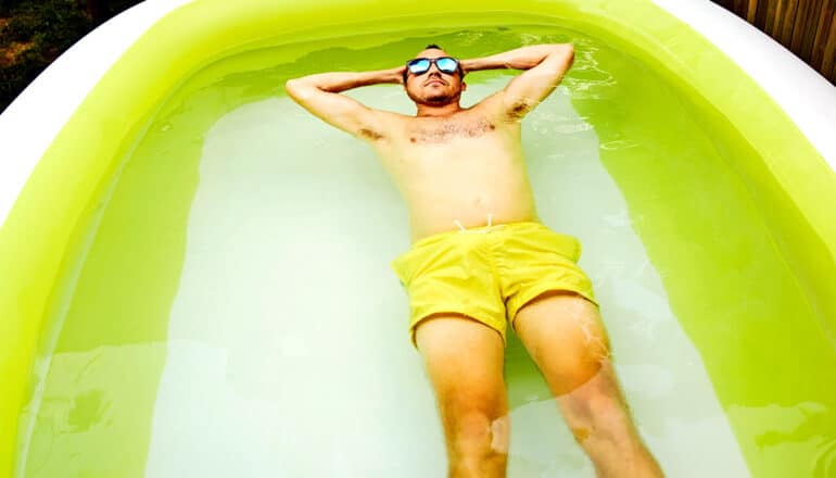 A man lays back in a white and lime green inflatable pool.