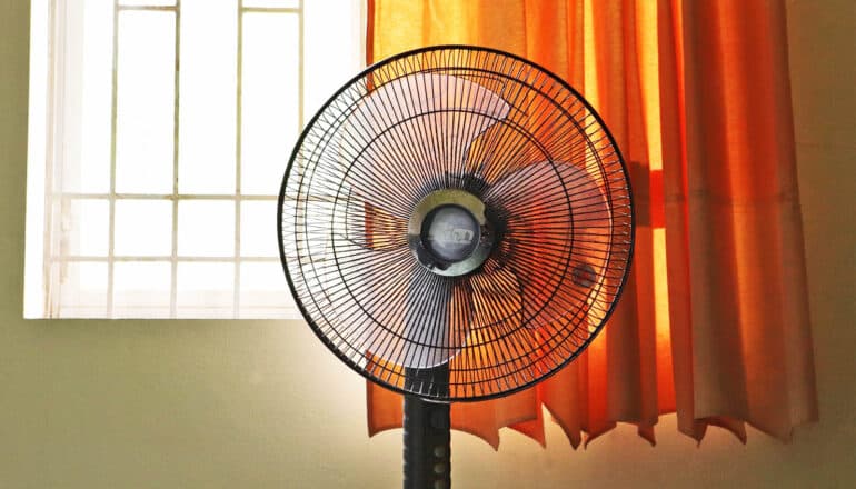 fan in front of sunny window with orange curtain