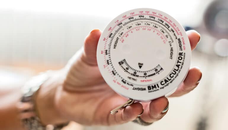 A person holds up a round plastic BMI calculator.