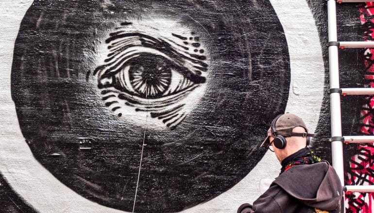 An artist paints an eye on a wall in black and white.