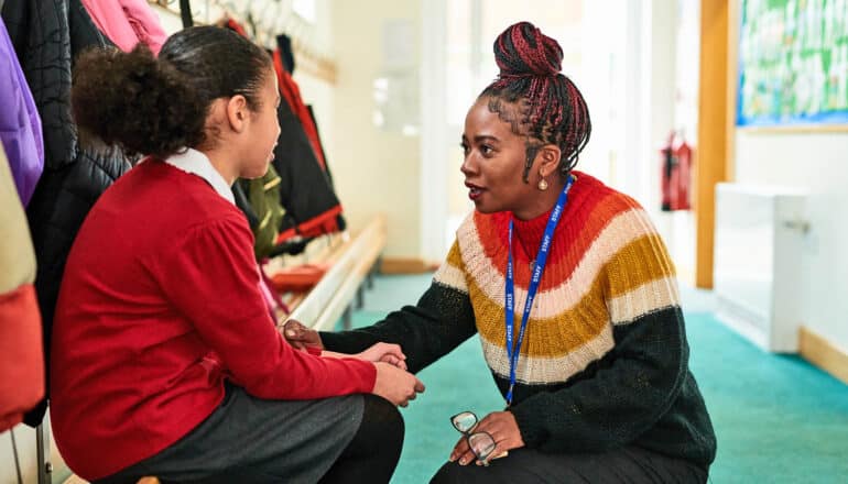 teacher kneels to speak with student