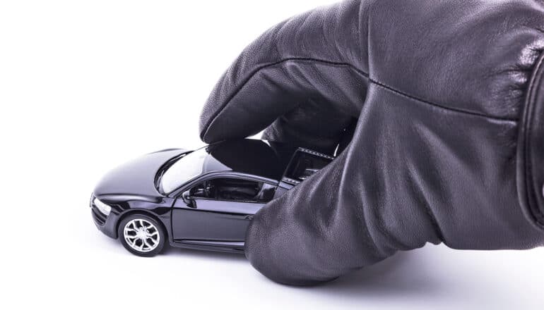 A gloved hand picks up a toy car on a white background.