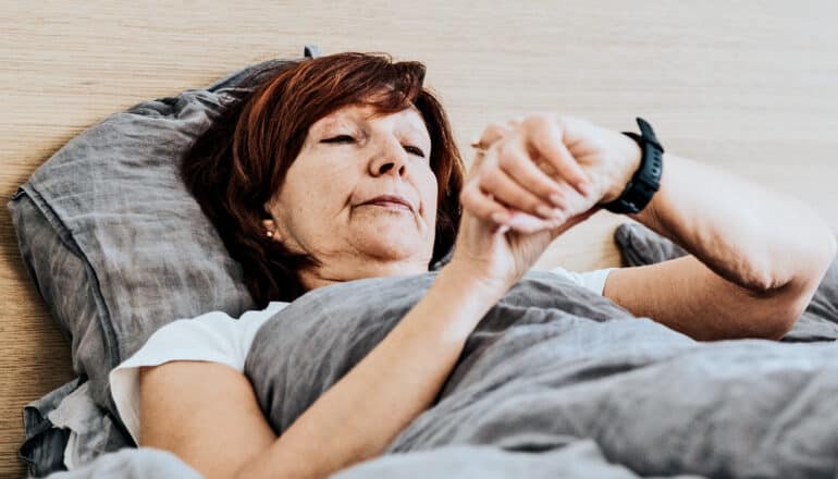 A woman looks at her Fitbit while laying in bed.