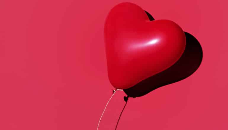 A heart-shaped balloon floating away against a red background.