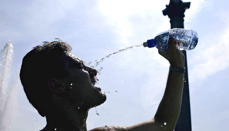 A man squirts a water bottle into his face while outside in the heat.