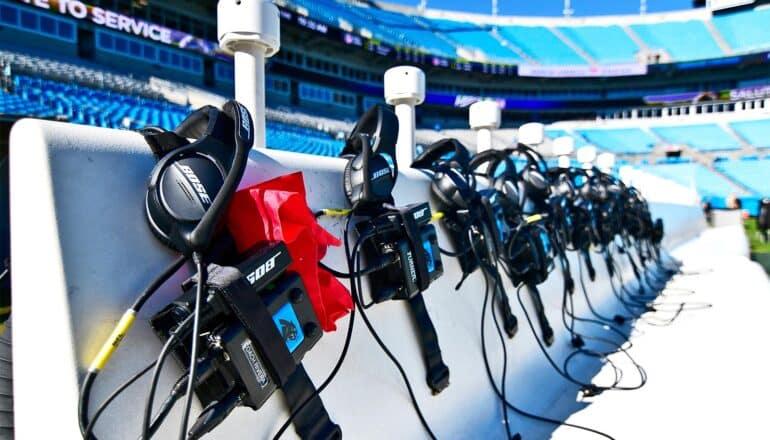 Coaching headsets rest on the sideline bench in an empty stadium ahead of an NFL game.