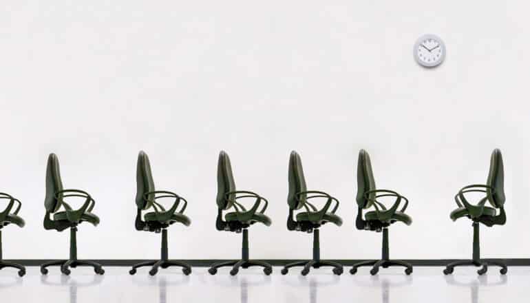 row of office chairs beneath clock on white wall