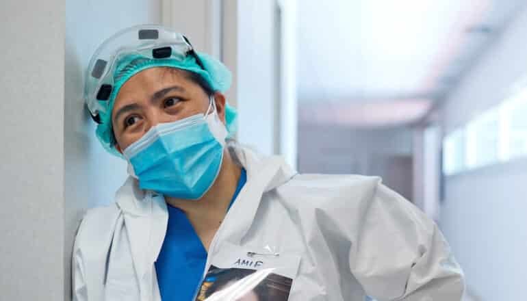 nurse in PPE leans against wall