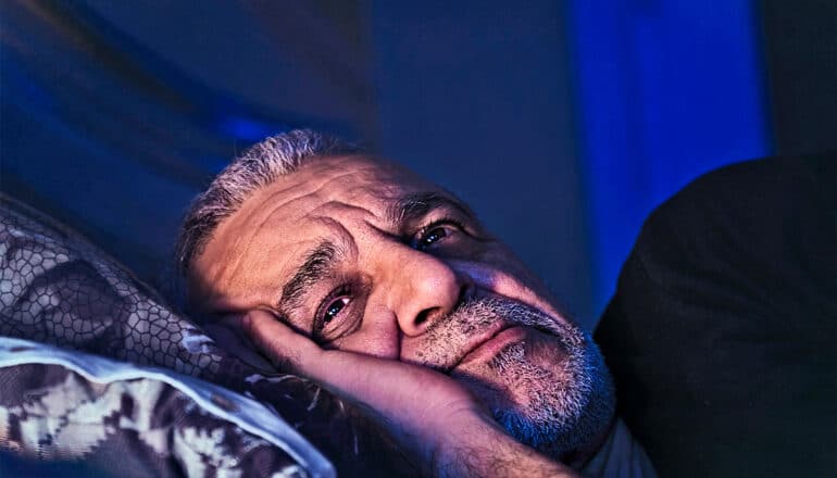 An older man lays in bed awake.