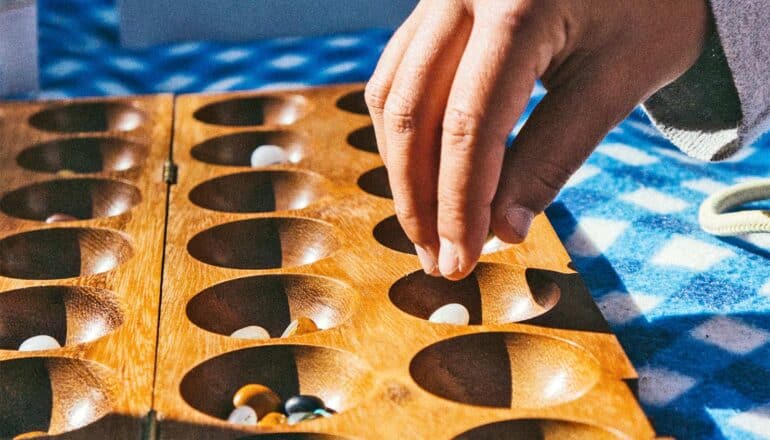 A person places stones in a mancala board.