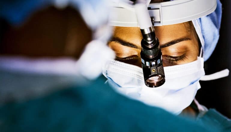 A female surgeon looks down with a face mask and headlamp on.