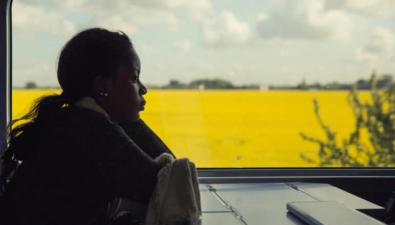 person sits in front of window, yellow field visible behind them