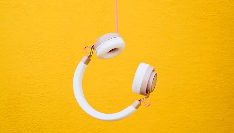 A pair of headphones dangles upside down against a yellow background.