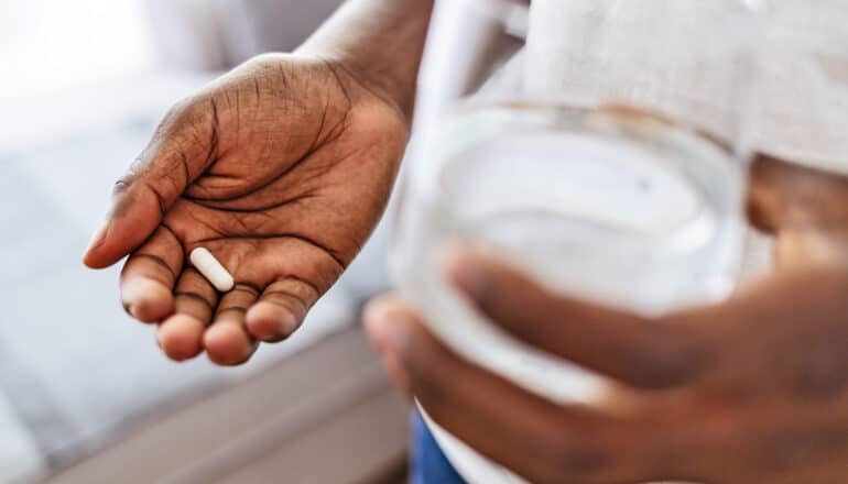 hands of person holding pill and glass of water