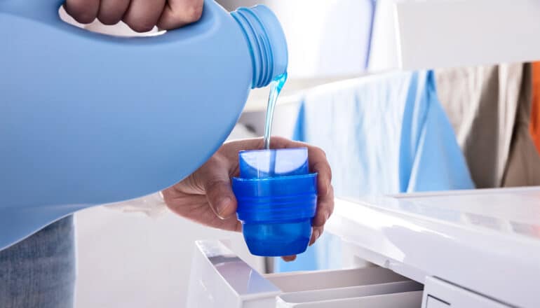 A person pours blue laundry detergent into the cap.