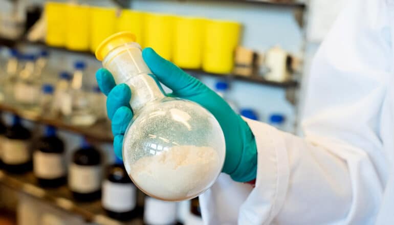 gloved hand holds stoppered glass bottle of white powder