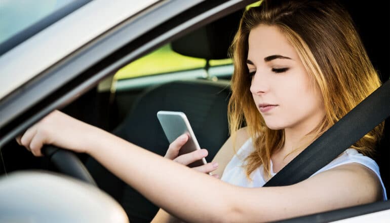 A young woman texting while driving.