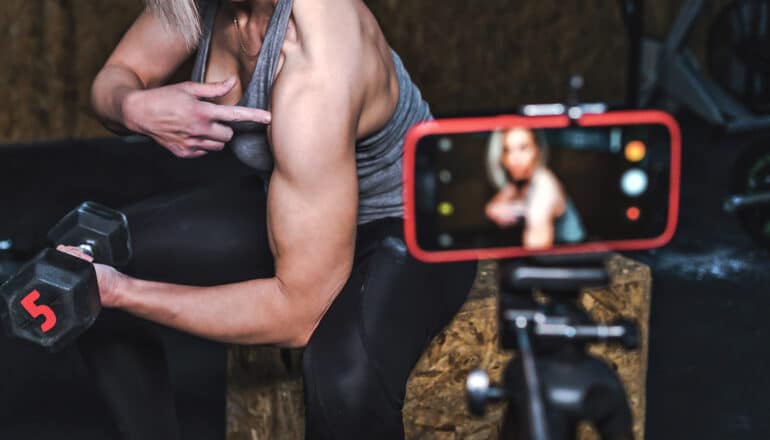 camera on tripod record person holding barbell and pointing at arm muscle