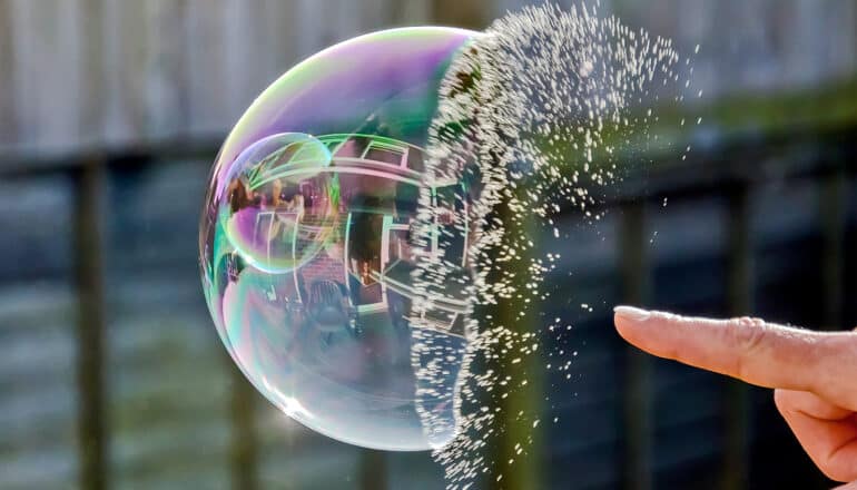 A person pops a soap bubble floating in the air outside.