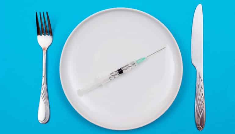 syringe on plate with fork and knife