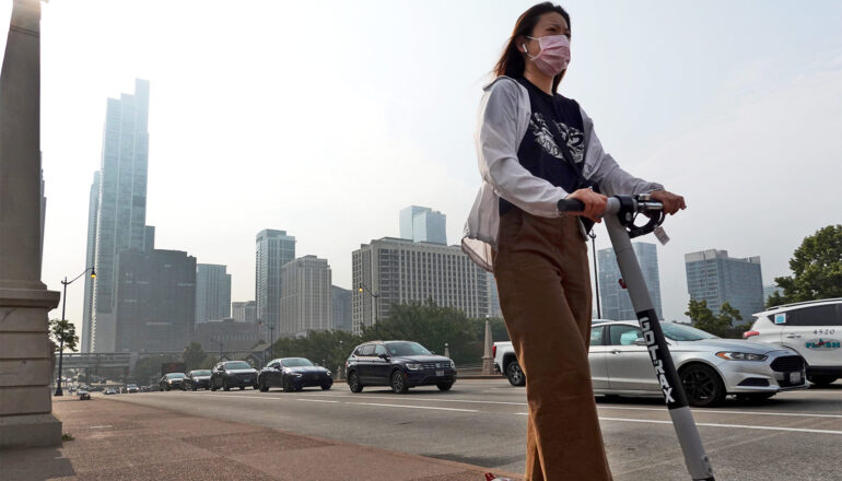 A woman rides a scooter through Chicago while wearing a facemask.