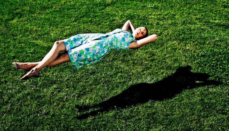 A sleeping woman hovers above a grassy field.