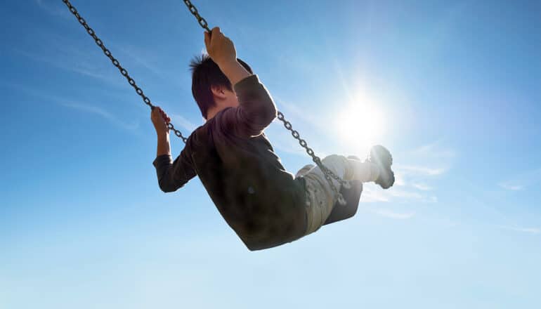 A young boy swings on a playset with the bright sun behind him.