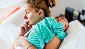 A mother looks off into the distance with her baby on her shoulder.