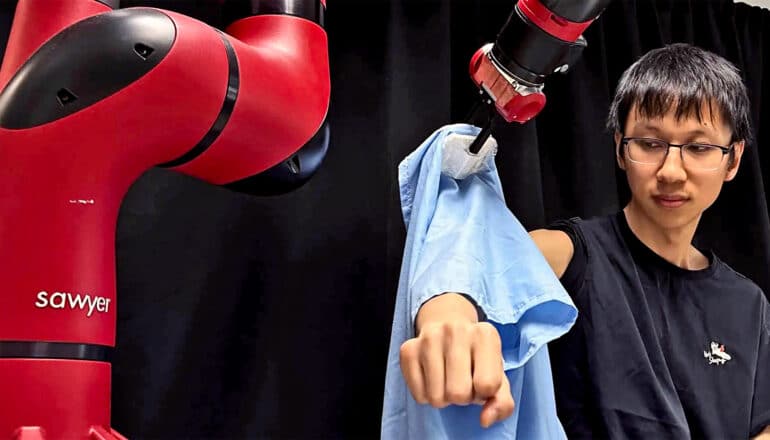 A researcher holds out his arm as a robot arm pulls a shirt onto his body.