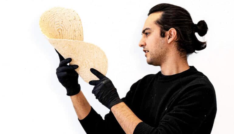 Khan holds a bent piece of the 3D-printed, sawdust-based building material.