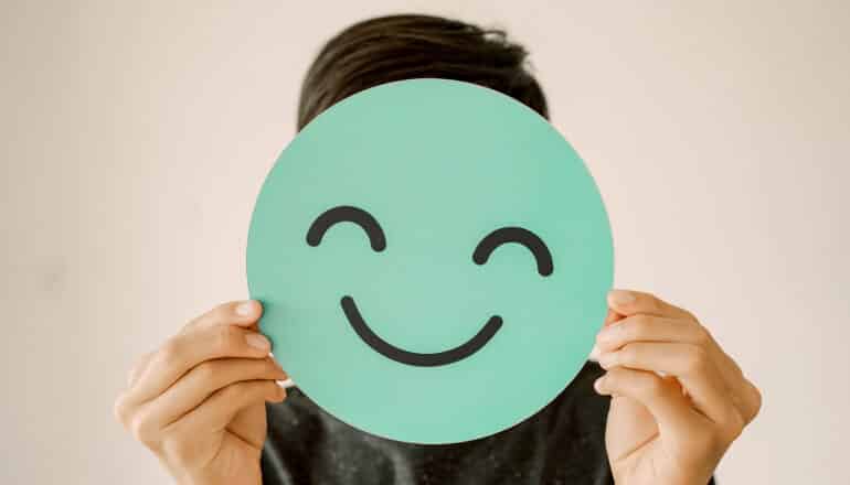 person holds round green smiley face in front of their head