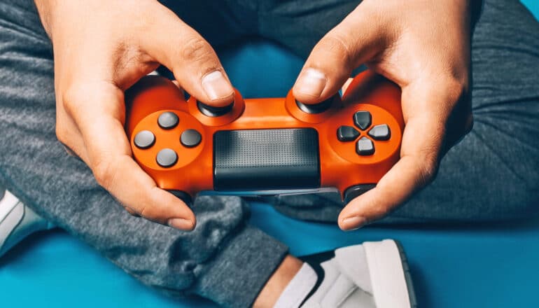 A young man holds an orange video game controller.