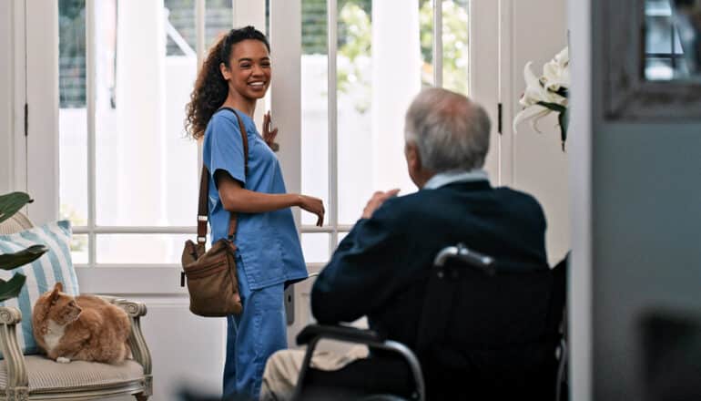 nurse at door of home, smiling at older adult in wheelchair