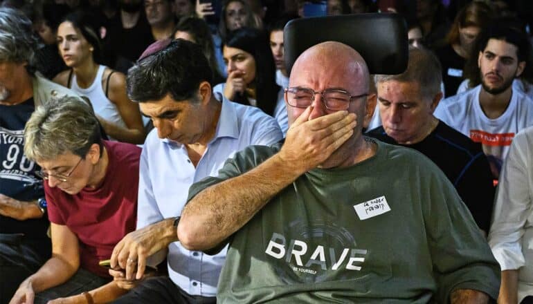 A man cries and covers his mouth while sitting in a crowd.