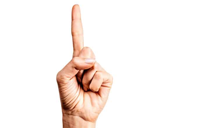 A person holds up their index finger indicating the number one against a white background.