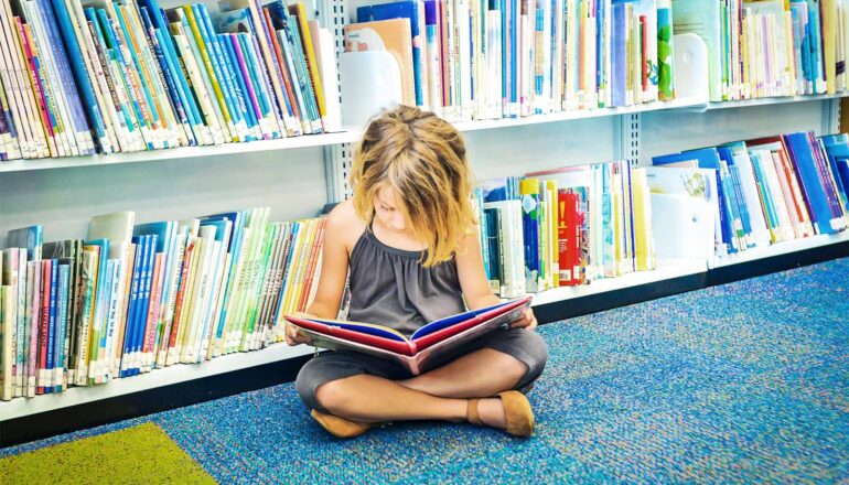 A lone girl reads books in a children's school library.