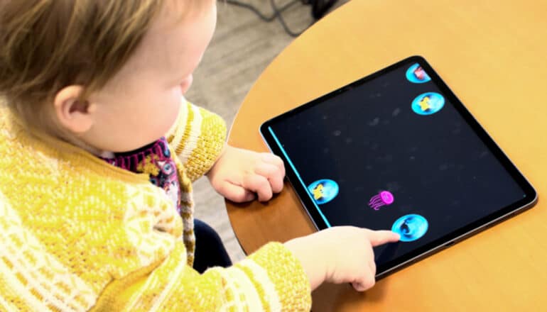 A young child plays a tablet game while sitting at a table.