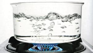 A clear pot of boiling water over a gas stove.