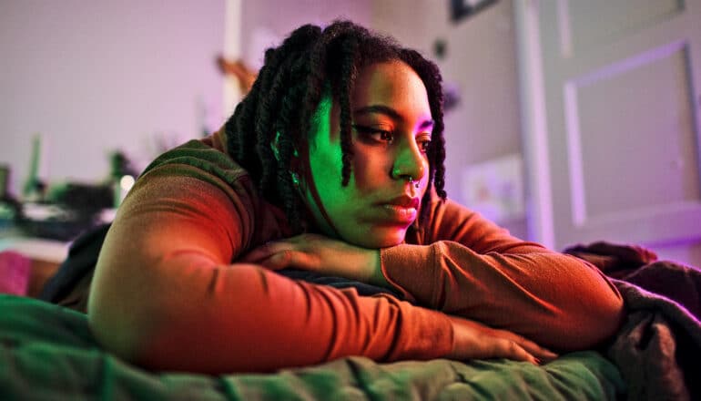 A young woman lays on her bed alone.