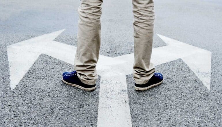 A man stands on asphalt over painted arrows pointing in opposite directions.