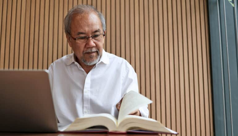 older adult with book and laptop