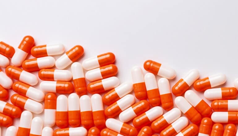 Many orange and white capsules on a white background.