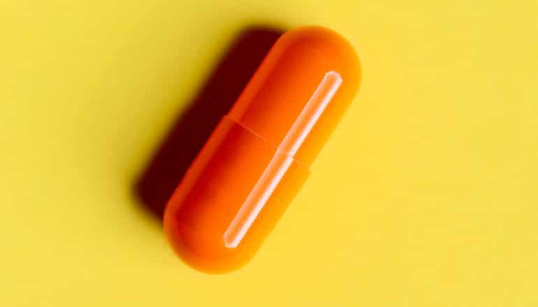 An orange capsule sitting on a yellow background.