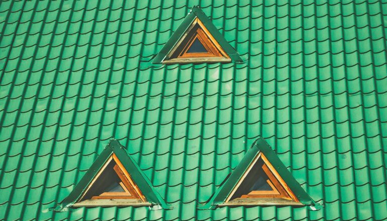 Three small windows in a green tiled roof.