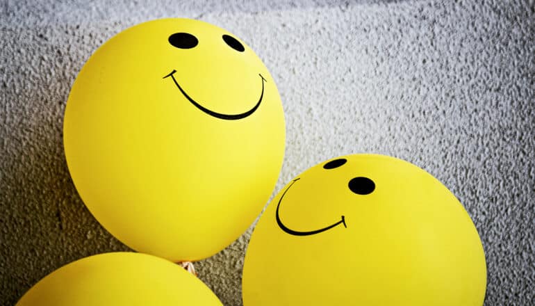 Yellow balloons with smiley faces on them against a stucco background.