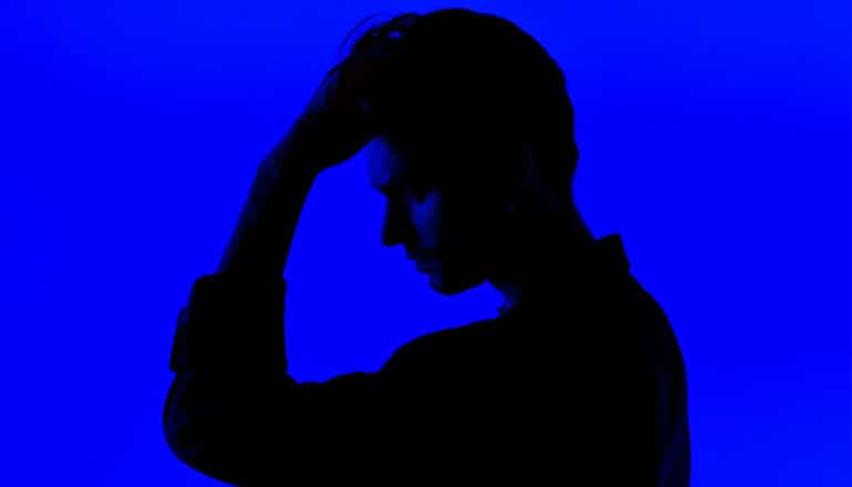 A young man in profile and silhouette holds his forehead.