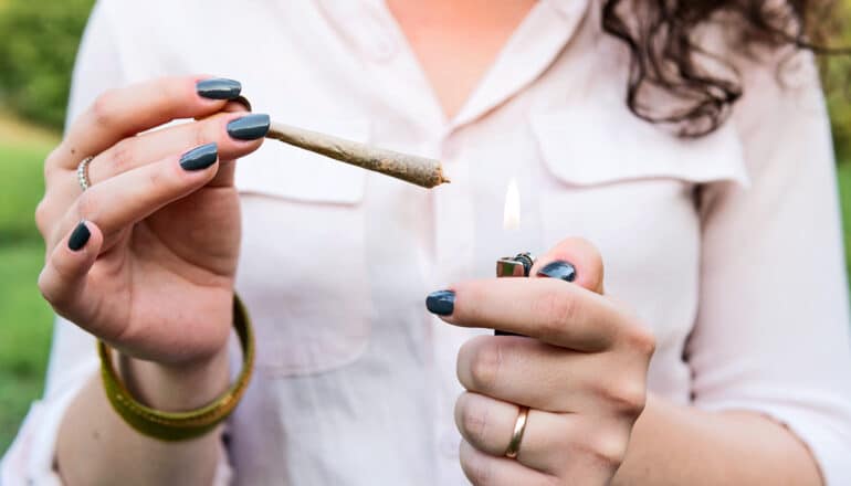 A young woman holds a joint in one hand and a lighter in the other.