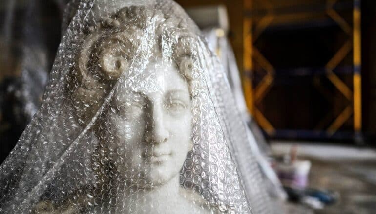 A marble bust under bubble wrap in a dark room.