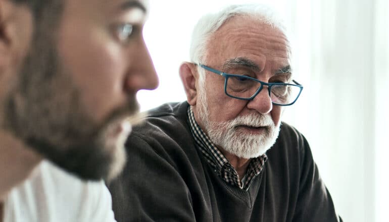 An older man looks concerned while sitting next to his adult son.